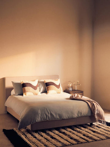 Modern upholstered bed with neutral bedding, patterned cushions and throw in styled bedroom