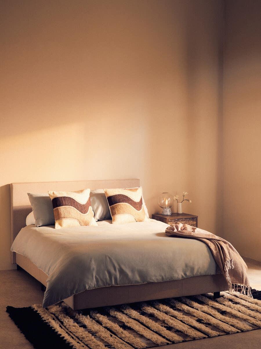 Modern upholstered bed with neutral bedding, patterned cushions and throw in styled bedroom