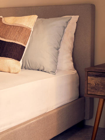 Beige upholstered bed with neutral cushions beside a wooden bedside table