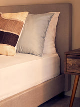 Beige upholstered bed with neutral cushions beside a wooden bedside table