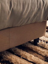 Fabric bed base corner with grey bedding on textured beige and brown rug