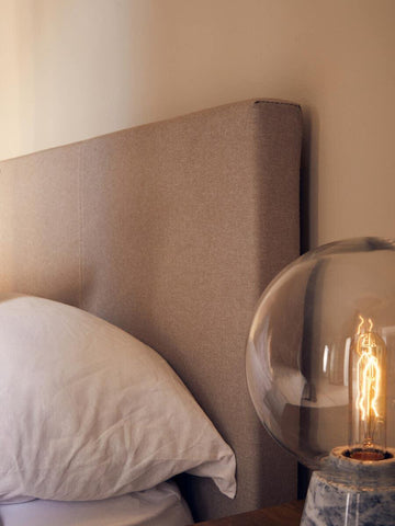 Beige upholstered bed headboard with white pillow and marble table lamp near bedside