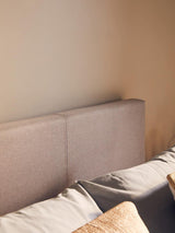 Beige fabric bed headboard with stitched detail and neutral bedding in bright bedroom