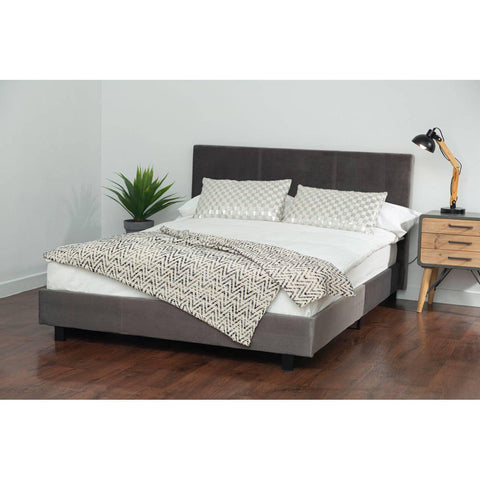 Grey upholstered bed frame with headboard, patterned bedding, and bedside table