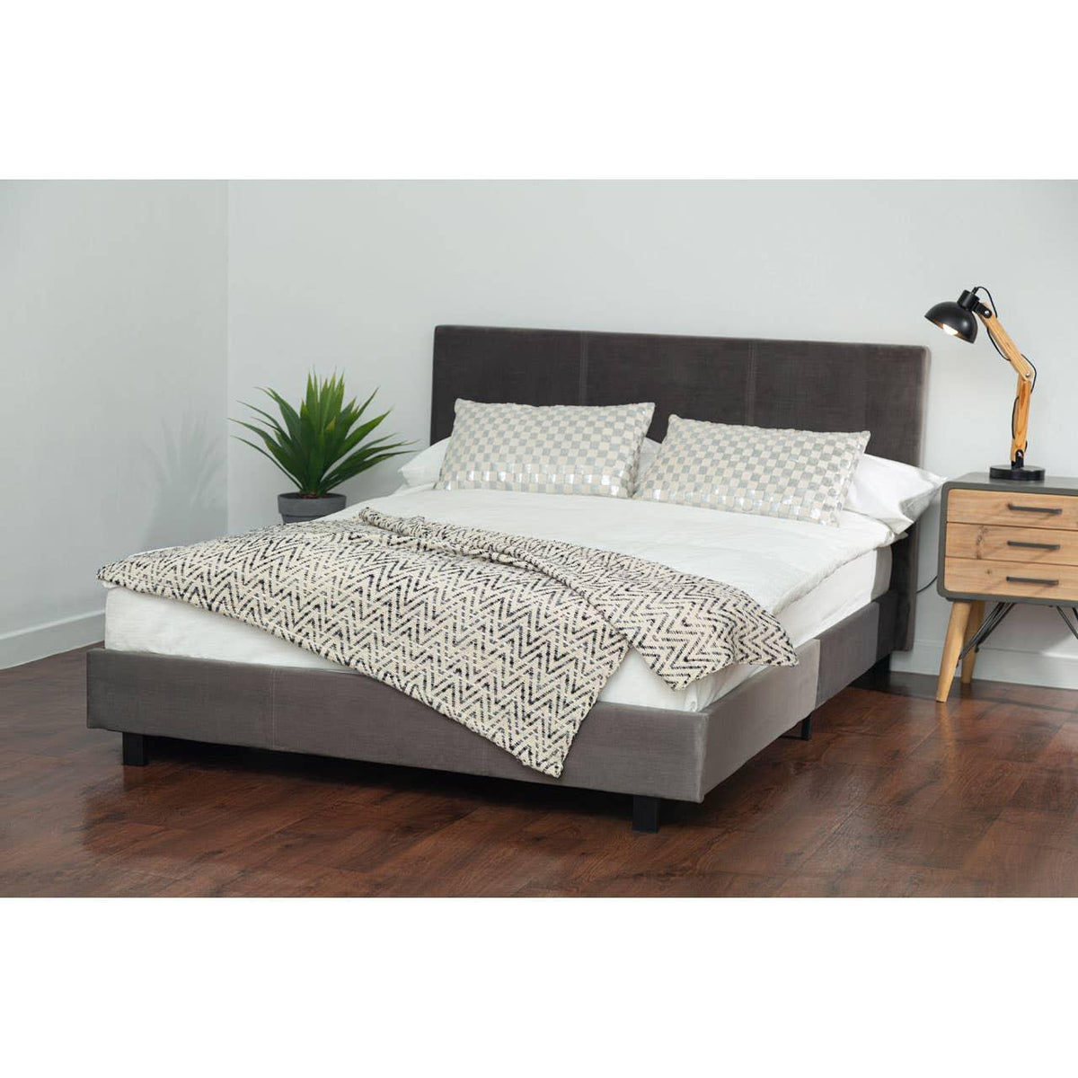 Grey upholstered bed frame with headboard, patterned bedding, and bedside table