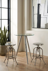 Round glass bar table with chrome legs positioned between two matching bar stools, set against a backdrop of large windows and a mirror, with a potted plant nearby on a wooden floor
