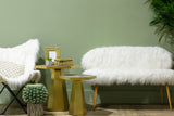Sienna white faux fur two-seat sofa with gold finish legs positioned next to a matching white faux fur chair, accompanied by two gold accent tables. The background features a soft green wall and a potted plant, creating a cozy and modern living space