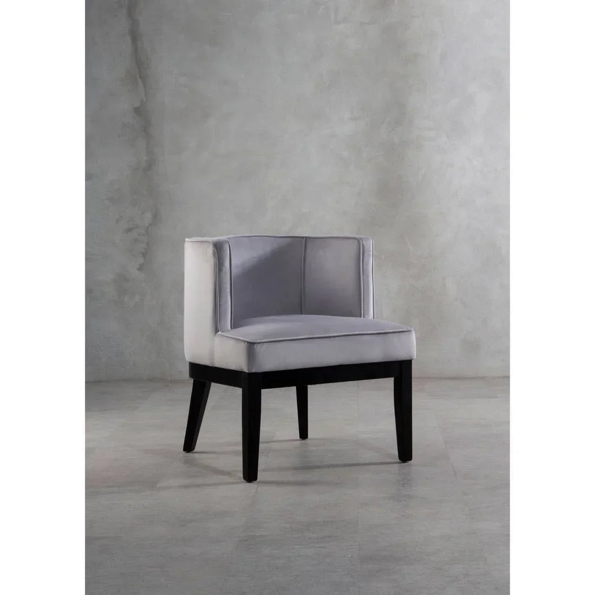 Grey velvet accent chair with panelled backrest and black wooden legs on concrete floor