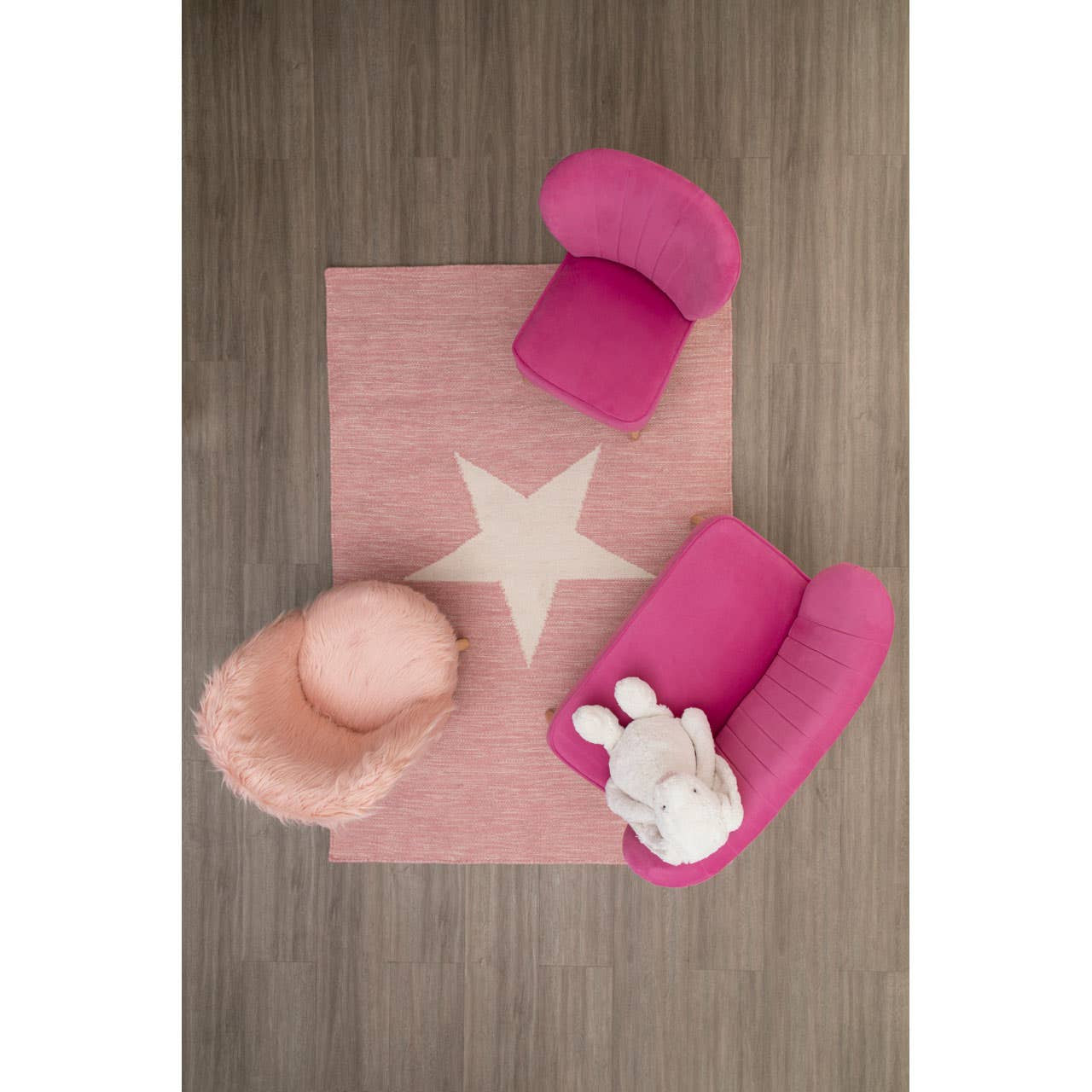A cozy kids' pink faux fur chair positioned on a light pink rug with a white star design, alongside a fluffy pink pouf and a plush white bunny toy, all set against a wooden floor