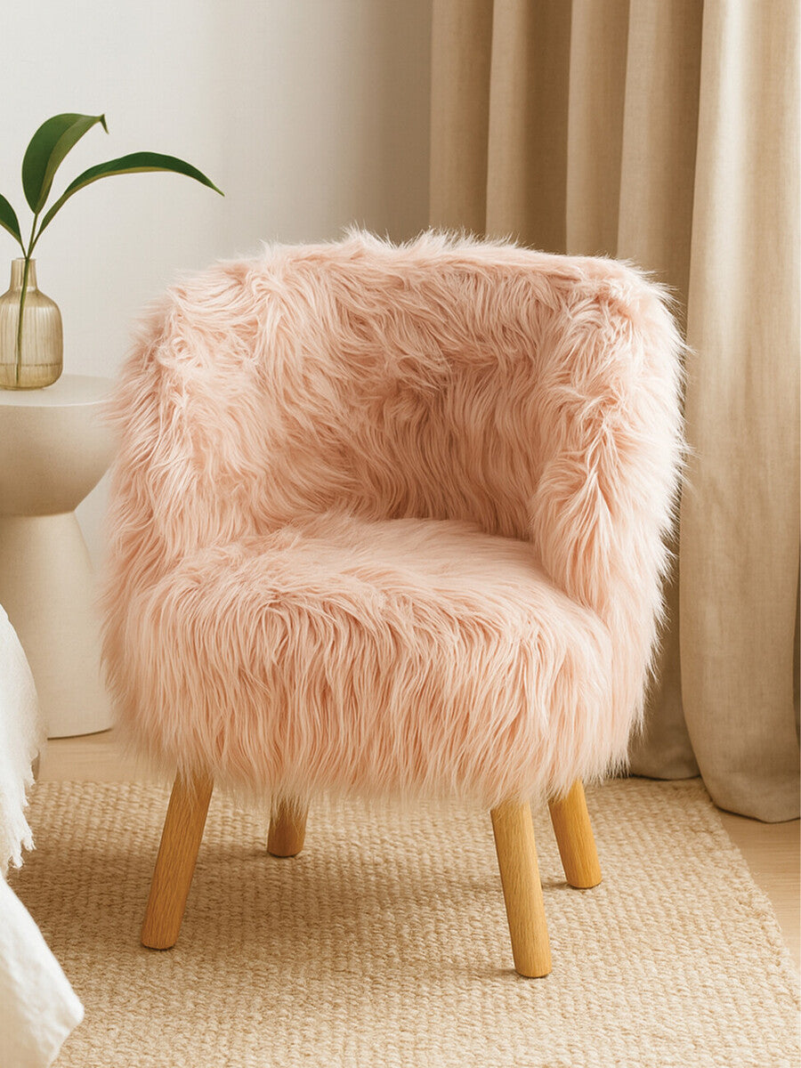 Soft pink faux fur chair with a rounded backrest and wooden legs, placed on a light-colored rug next to a small table and a potted plant. Natural light filters through nearby curtains, creating a cozy atmosphere