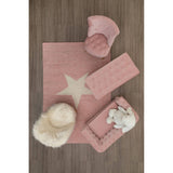 A cozy kids' white faux fur chair placed on a soft pink rug featuring a star design, surrounded by a pink storage box and a fluffy white pouf, all set against a wooden floor