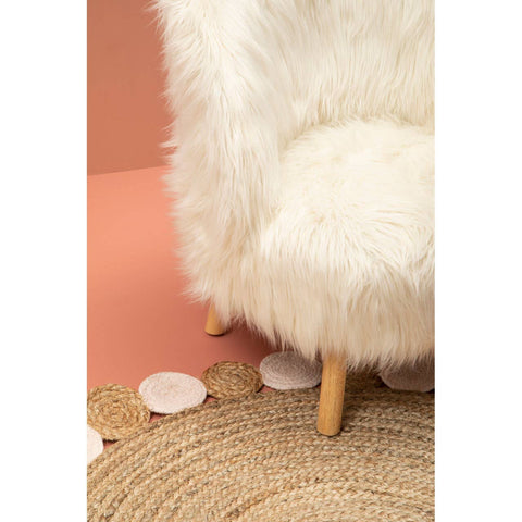 A cozy white faux fur chair with wooden legs, positioned on a textured round rug, against a soft pink background. The chair features a plush seat and backrest, creating a comfortable and inviting look for a child's room