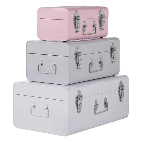 Set of three metal storage trunks in pink, grey, and white stacked on white background