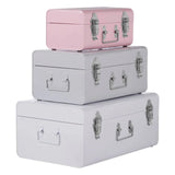 Set of three metal storage trunks in pink, grey, and white stacked on white background
