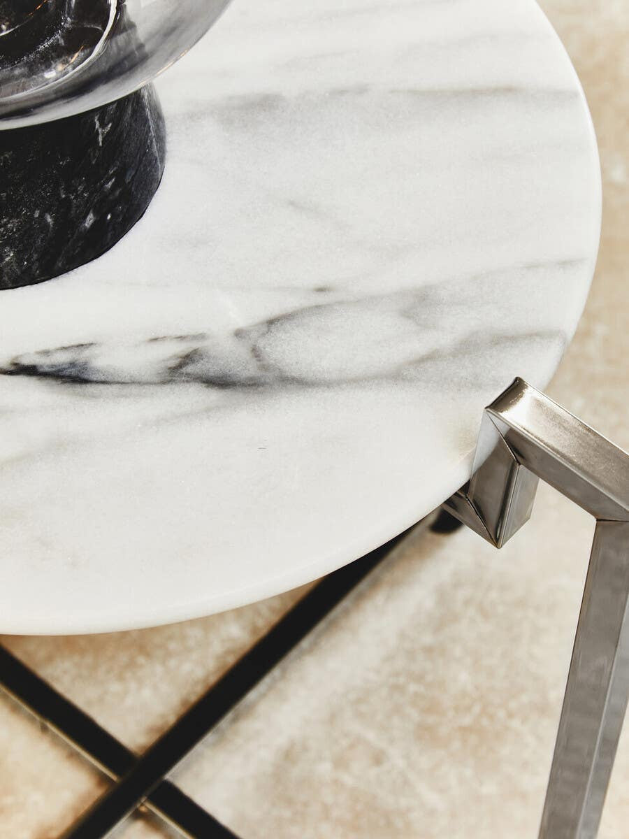 White marble side table featuring a sleek chrome base, showcasing a smooth, polished surface with subtle gray veining. The table is positioned on a light-colored floor, with a decorative item placed on top, highlighting its modern design