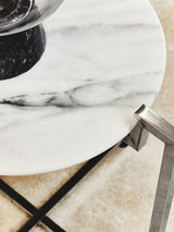 White marble side table featuring a sleek chrome base, showcasing a smooth, polished surface with subtle gray veining. The table is positioned on a light-colored floor, with a decorative item placed on top, highlighting its modern design