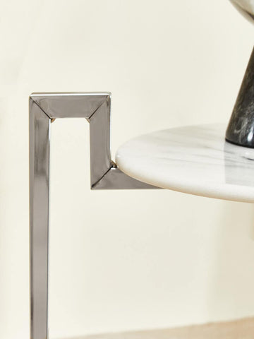 A close-up view of a white marble side table featuring a sleek chrome base, showcasing the elegant design and smooth surface of the marble alongside the modern geometric shape of the chrome support