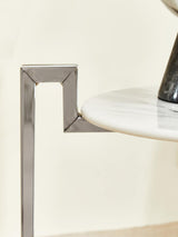 A close-up view of a white marble side table featuring a sleek chrome base, showcasing the elegant design and smooth surface of the marble alongside the modern geometric shape of the chrome support
