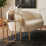 A white marble side table with a warm gold base, positioned next to a light-colored curved sofa. The table features a round top and slender legs, complementing the modern decor. A decorative vase with white flowers sits on the table, enhancing the elegant aesthetic of the room. The background includes a dark rug and a piece of artwork on the wall