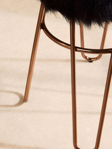 Faux fur stool with a rose gold finish, featuring slender metal legs and a plush black seat, set against a light wooden floor