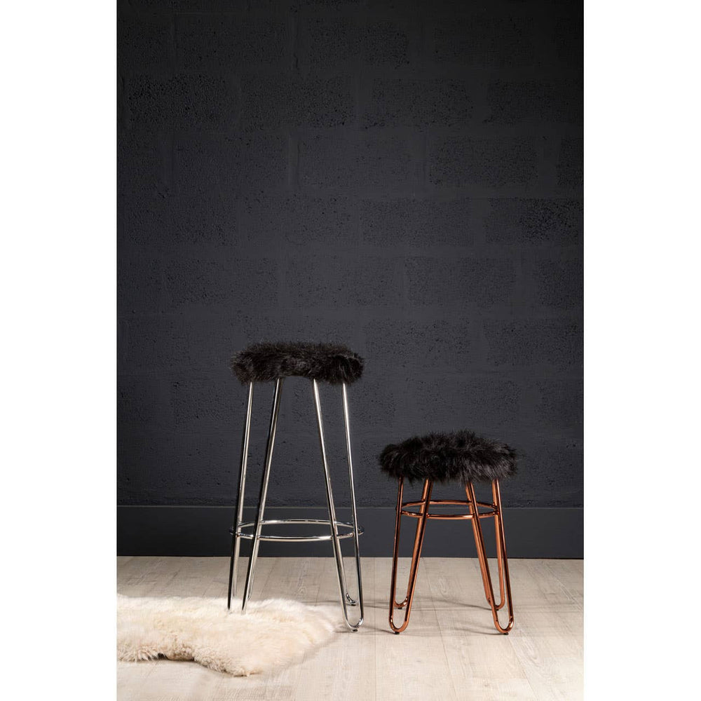 Faux fur stool with a rose gold finish, featuring a plush black seat and slender metal legs, positioned next to a taller stool against a dark wall, with a light-colored rug underneath
