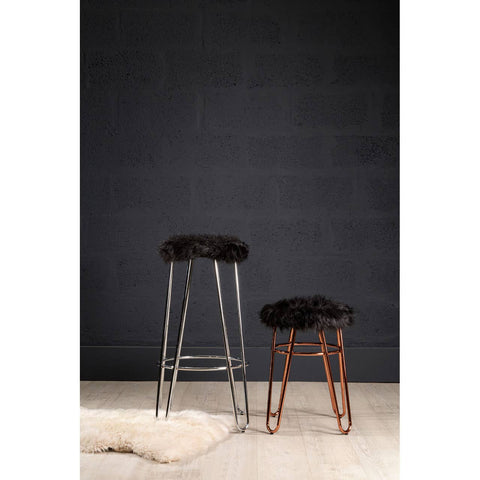Faux fur stool with a rose gold finish, featuring a plush black seat and slender metal legs, positioned next to a taller stool against a dark wall, with a light-colored rug underneath