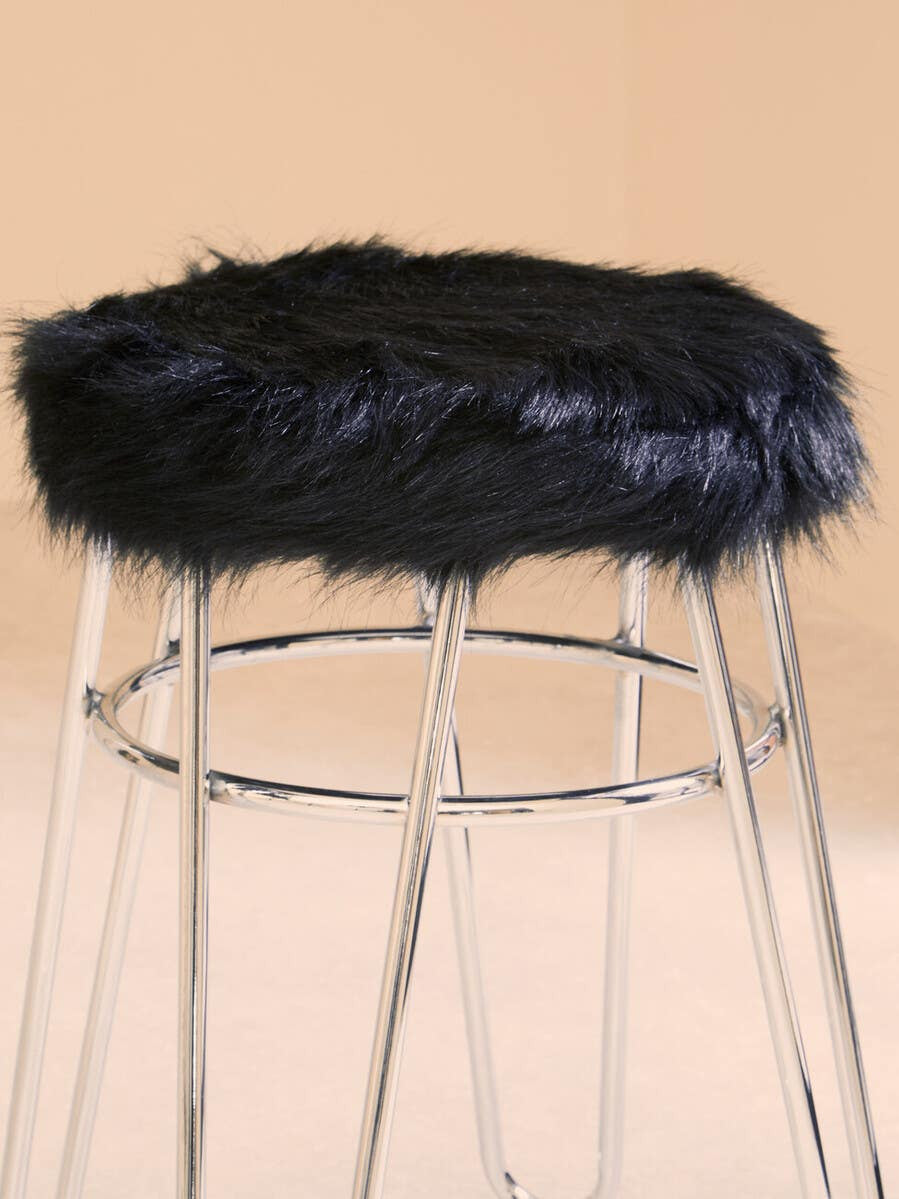 Black faux fur stool with a plush top resting on a sleek, metallic frame. The stool features a minimalist design with slender legs, creating a modern aesthetic. The background is a soft, neutral color that complements the stool