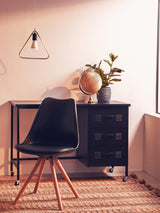 Black padded seat dining chair with a sleek design, positioned next to a wooden side table. The chair features a modern silhouette and wooden legs. A decorative globe and a potted plant are placed on the table, with a wall-mounted light fixture in the background. The setting has warm lighting and a textured rug on the floor