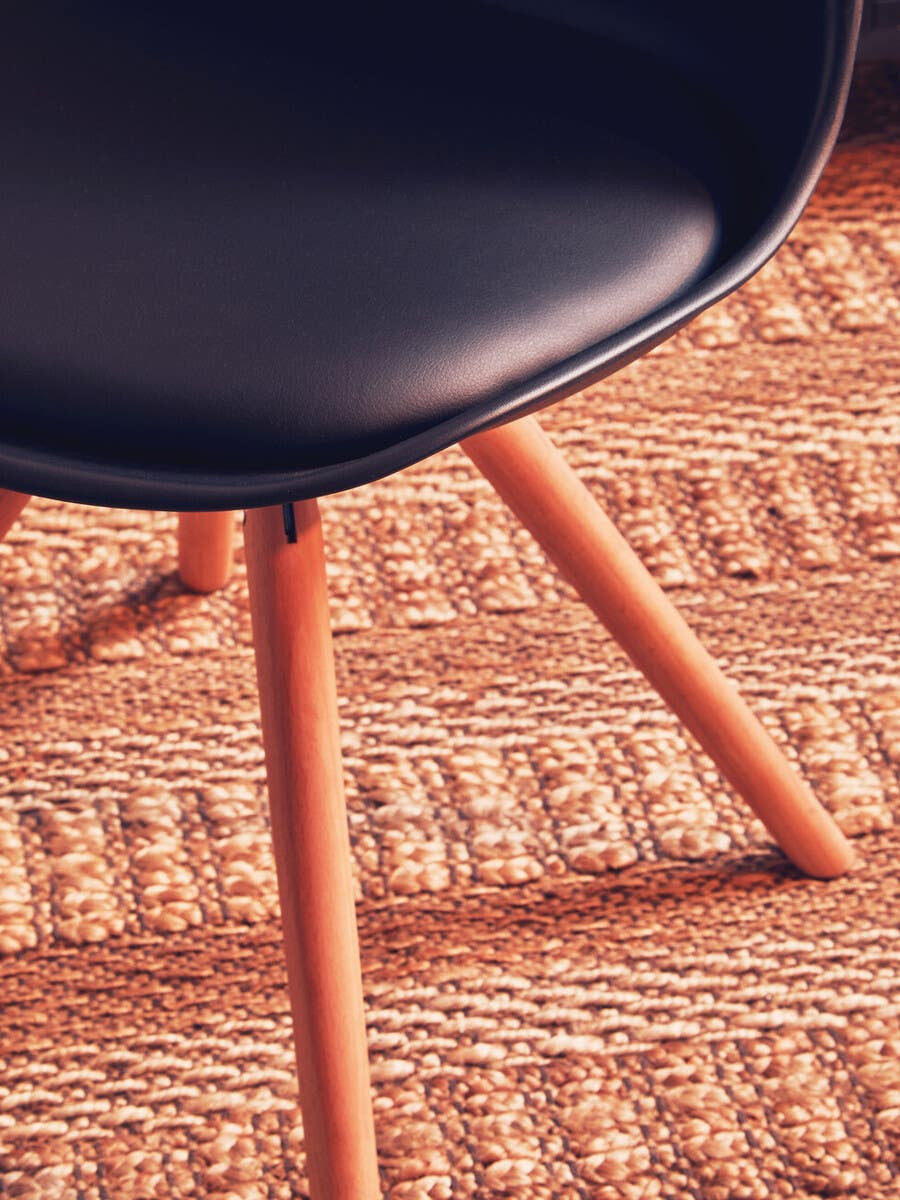 Black padded seat dining chair with wooden legs, positioned on a textured woven rug. The chair features a smooth, rounded seat and slender, angled legs that provide a modern aesthetic