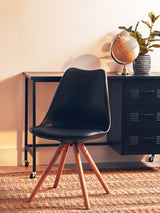 Black padded seat dining chair with a sleek, curved backrest and wooden legs, positioned next to a console table in a cozy interior setting. A globe and a plant are visible on the table, with a textured rug beneath the chair