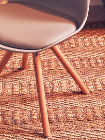 Modern dining chair with light wood legs and beige seat on woven rug