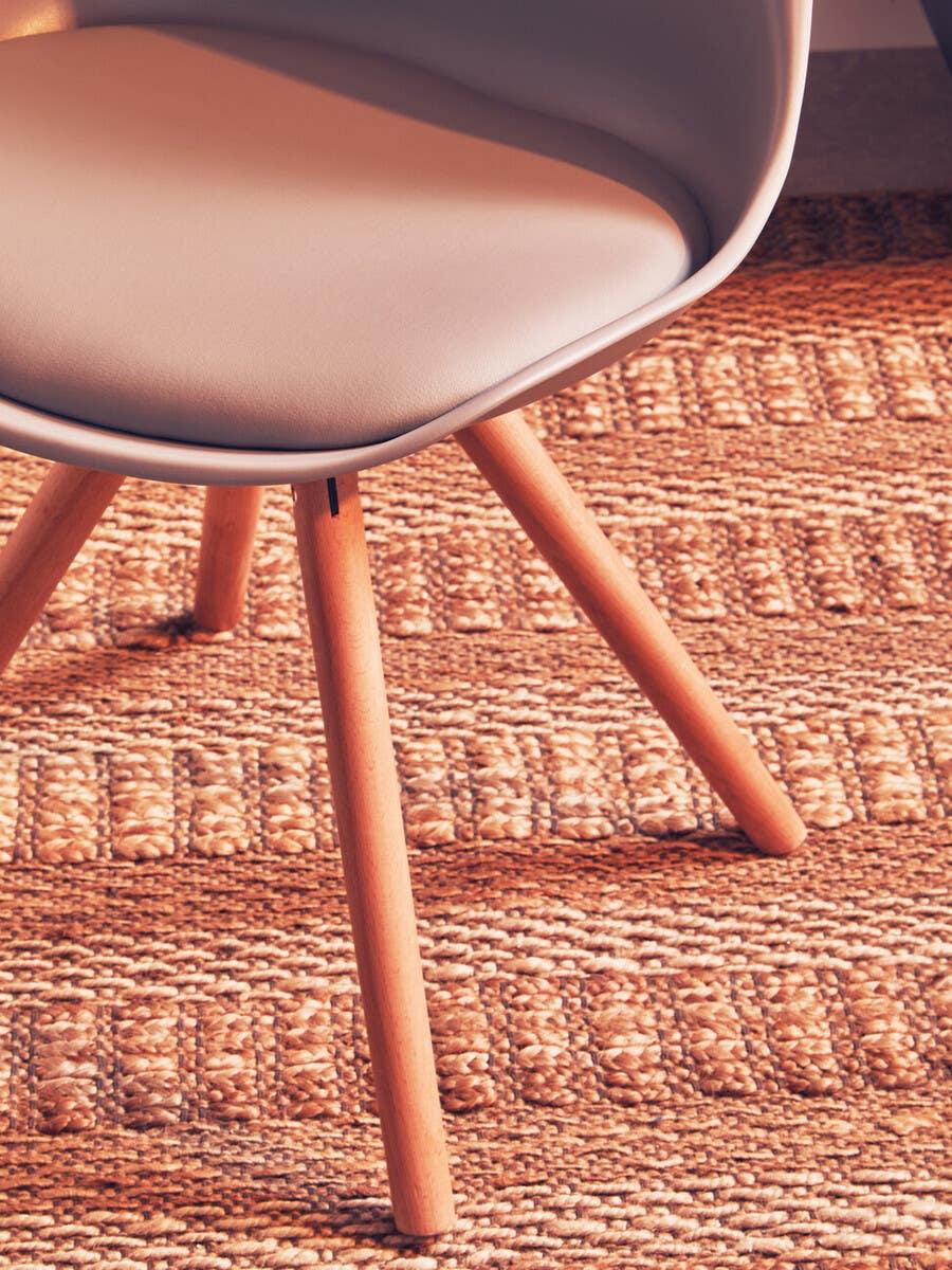 Modern dining chair with light wood legs and beige seat on woven rug
