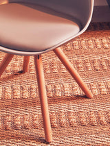 Modern dining chair with light wood legs and beige seat on woven rug
