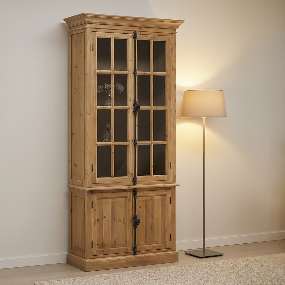 Tall cabinet made of pine wood featuring four doors with glass panels on the upper section and solid wood panels on the lower section. The cabinet has a natural wood finish, showcasing its grain, and is positioned against a light-colored wall next to a modern floor lamp