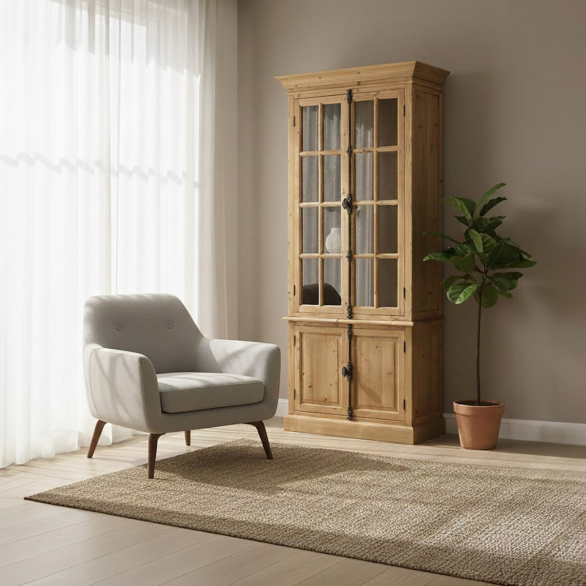 A tall cabinet made of pine wood with four glass doors, showcasing a natural wood finish. The cabinet is positioned next to a light gray armchair on a beige rug, with a potted plant in the background and soft natural light filtering through sheer curtains. The wall behind is a neutral color, enhancing the warm tones of the furniture