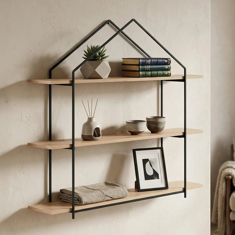 Three-tier wooden wall shelves with a black metal frame designed in a house shape, featuring natural wood shelves displaying a small potted plant, stacked books, and a framed picture, mounted against a light-colored wall