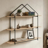 Three-tier wooden wall shelves with a black metal frame designed in a house shape, featuring natural wood shelves displaying a small potted plant, stacked books, and a framed picture, mounted against a light-colored wall