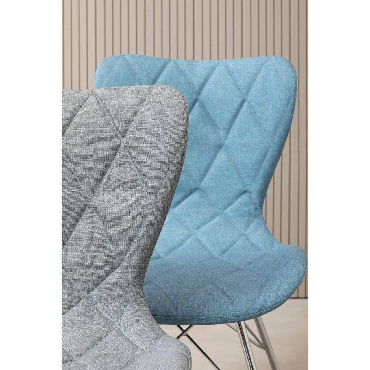 A blue dining chair with a quilted design, featuring a curved backrest and a sleek silhouette, positioned next to a light gray chair against a neutral background