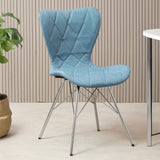 A stylish blue dining chair with a quilted fabric seat and backrest, supported by sleek metal legs, positioned next to a small round table and a potted plant in a modern interior setting