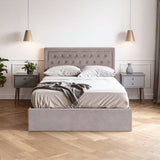 Grey velvet double ottoman bed with a tufted headboard, neatly made with white bedding and a dark throw blanket, positioned between two modern bedside tables with lamps, set against a light-colored wall and wooden floor