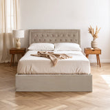 Mink velvet double bed with a tufted headboard, white bedding, and decorative throw draped across the top. The bed is positioned on a light wooden floor, accompanied by two wooden nightstands with a lamp and a vase of dried flowers. Soft natural light filters through sheer curtains in the background
