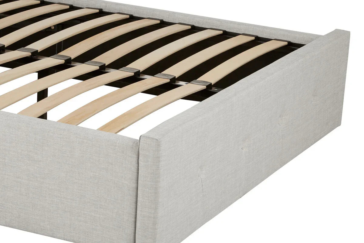 Light grey upholstered bed frame with wooden slats and low padded headboard, close view