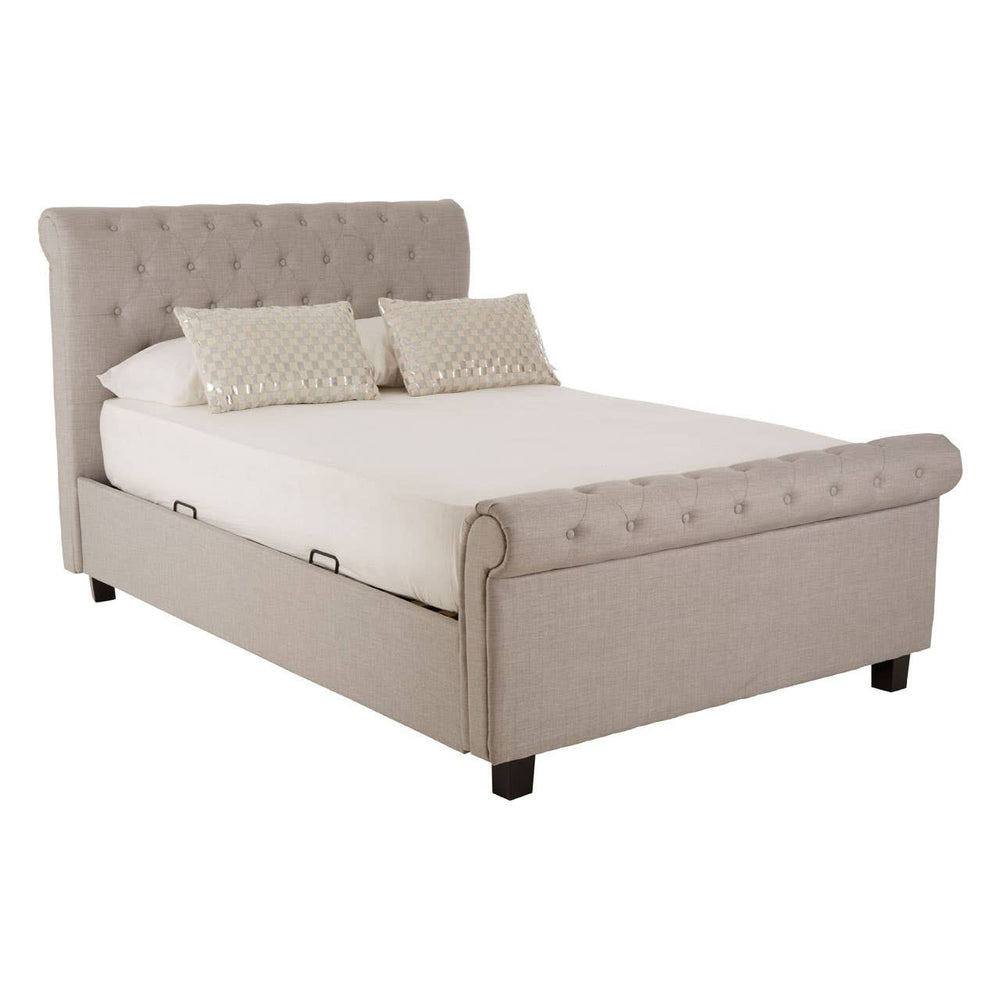 Light grey upholstered double bed with a tufted headboard, featuring two cream-colored pillows on a white mattress, resting on wooden legs. The design includes a storage ottoman feature at the foot of the bed