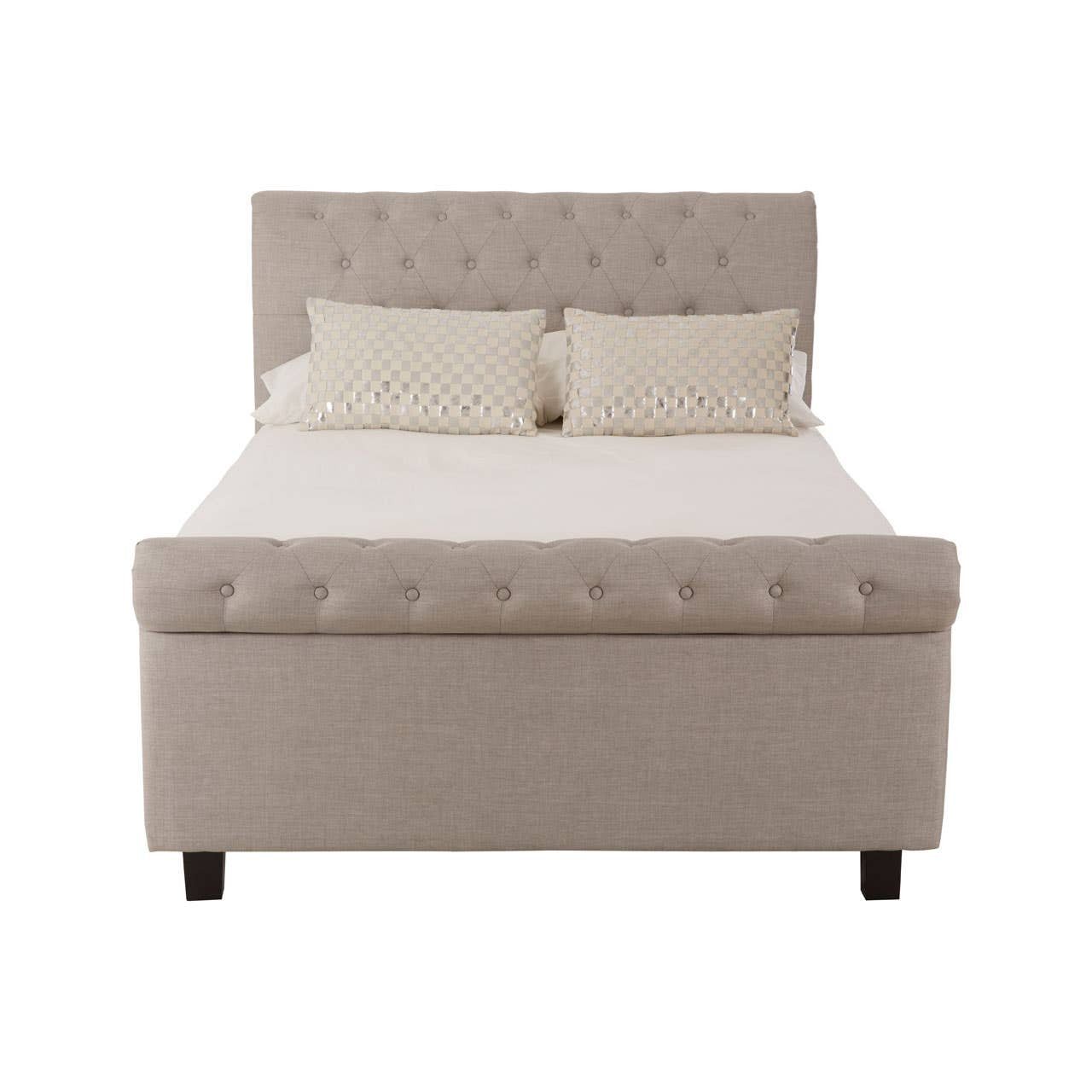 Light grey upholstered double bed with a tufted headboard, featuring two small decorative pillows on the mattress and a storage ottoman base. The bed stands on four black wooden legs