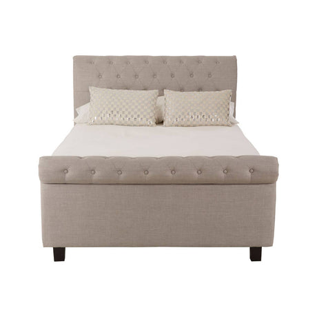 Light grey upholstered double bed with a tufted headboard, featuring two small decorative pillows on the mattress and a storage ottoman base. The bed stands on four black wooden legs