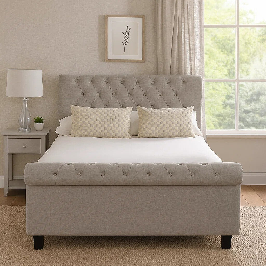 Light grey ottoman double bed with a tufted headboard, two cream-colored pillows, and a white mattress, positioned in a well-lit room with a window and a bedside table featuring a lamp