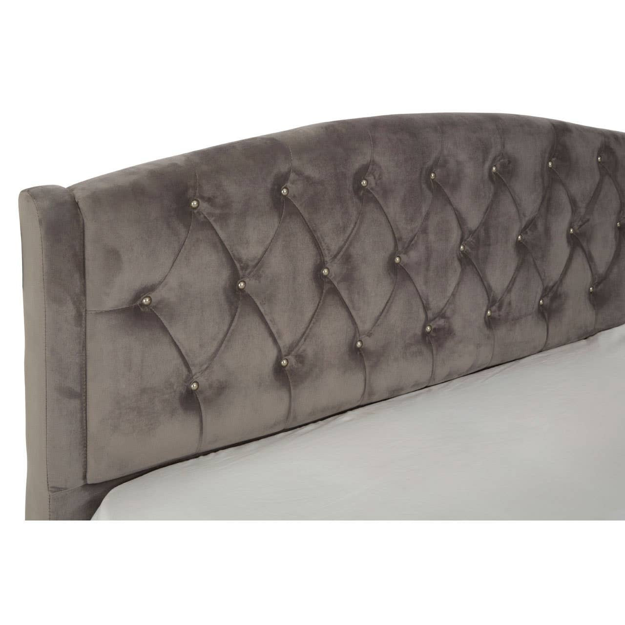 A tufted headboard in a soft steel shade, featuring a curved design and plush upholstery, with visible buttons creating a classic look. The bed frame is partially shown, emphasizing the elegant texture and color of the fabric