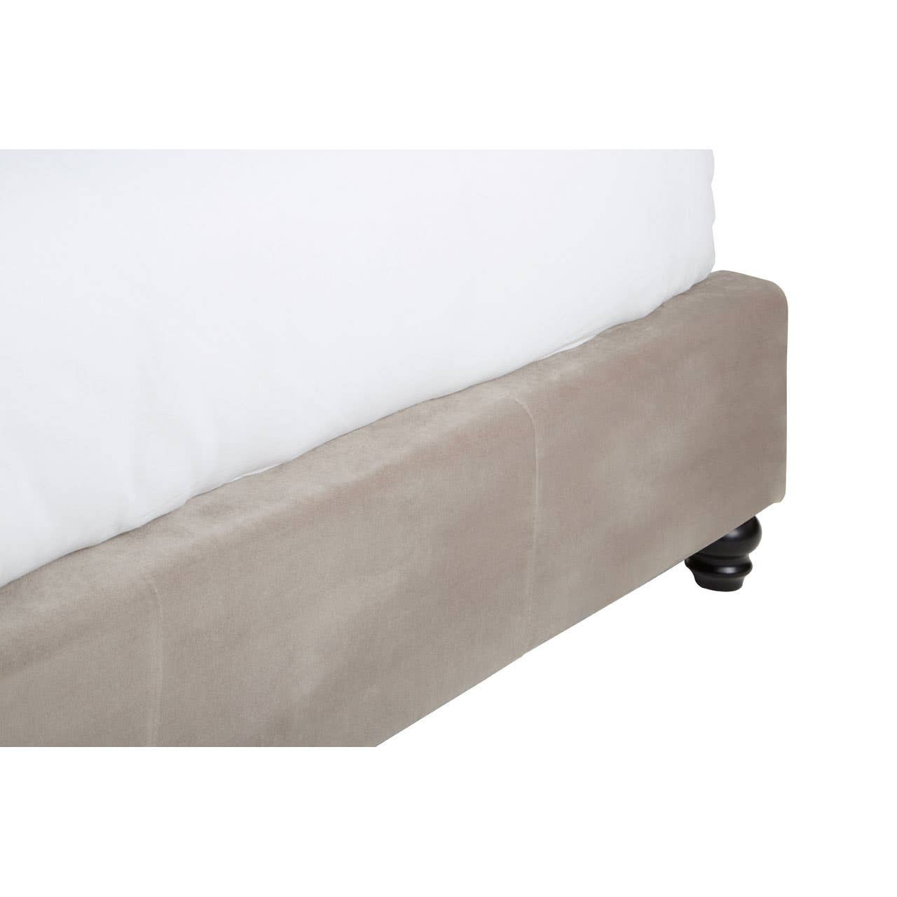 Mink brushed velvet fabric covers the base of a double bed, featuring a smooth texture and a subtle sheen. The bed has a low-profile design with a clean, modern aesthetic, and is supported by small black wheels for easy mobility. A white mattress and bedding are partially visible above the base