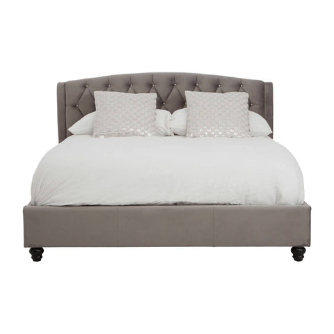 Grey velvet king bed with a tufted headboard, featuring two white decorative pillows and a white comforter, resting on dark wooden legs