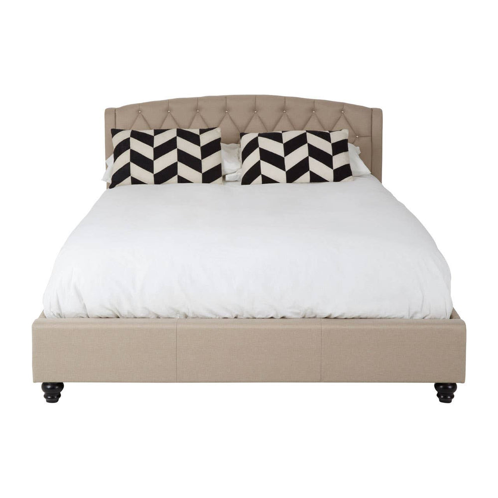 Beige king bed with a tufted headboard, featuring a white mattress and decorative black and white chevron-patterned pillows. The bed is supported by dark wooden legs